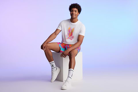 man on a blue background sitting with a white tee with a big bunny and a colorful swim