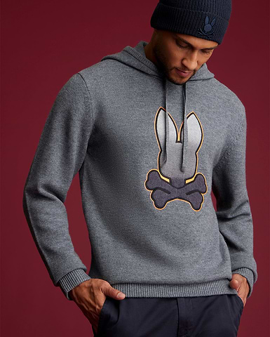 a man wearing a sweater in cashmere, grey sweater with a big psycho bunny logo in the middle. the man is also wearing a grey hat