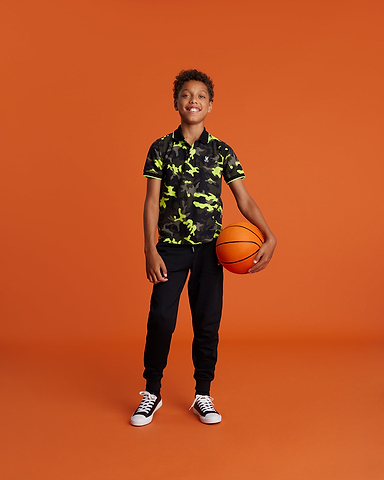 one kid standing with a boy camo polo shirt neon yellow and khaki with a basket ball in his hand