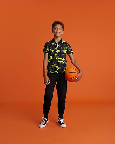 one kid standing with a boy camo polo shirt neon yellow and khaki with a basket ball in his hand