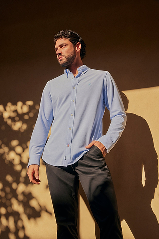 man looking on the left and wearing a long sleeve blue shirt and a navy chino, standing