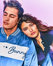 Mens Thomas Satin Bomber in two-tone blue satin with white chest stripe and embroidered Bunny script, alongside a dark blue pique polo with small white Psycho Bunny skull logo.