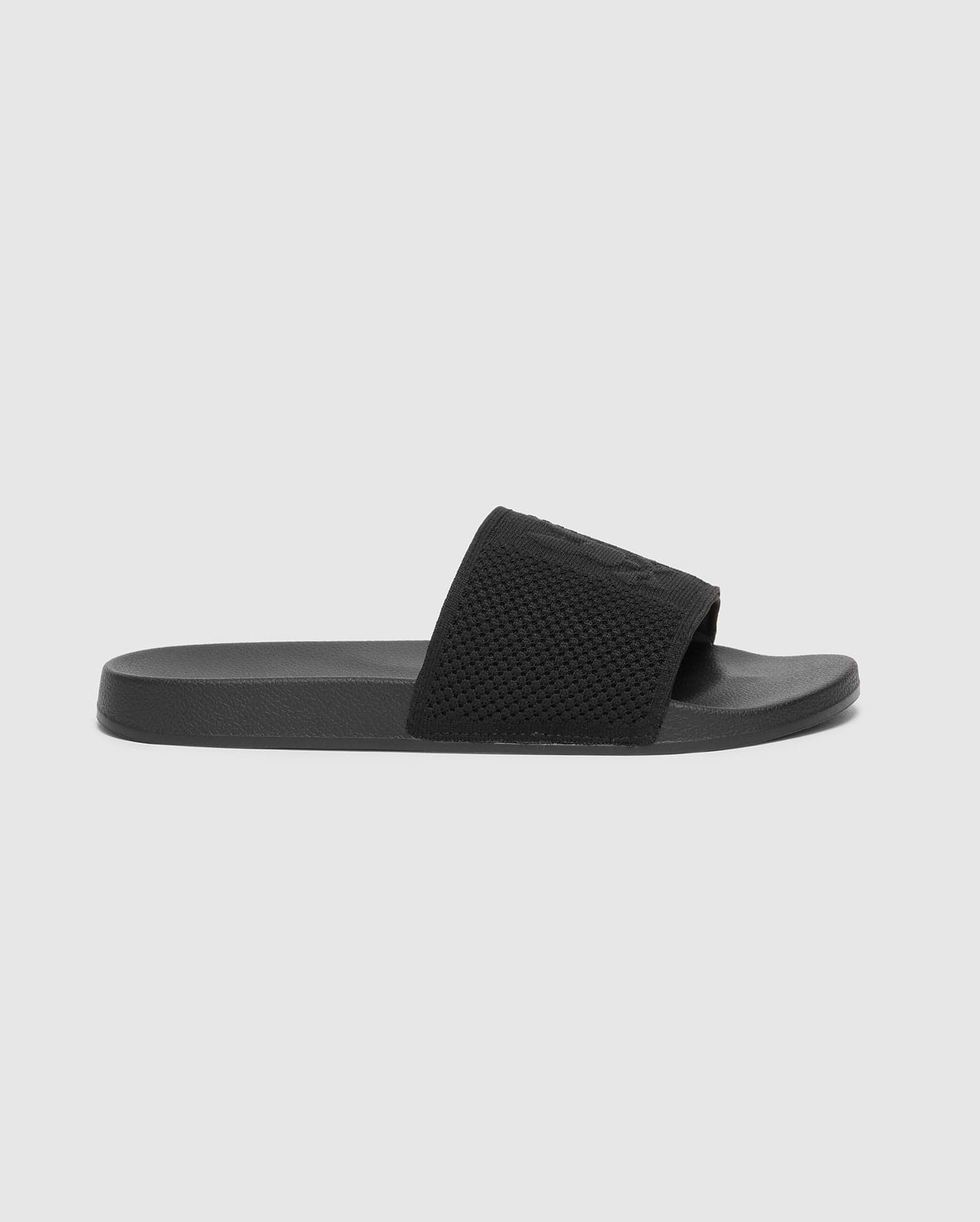 The Psycho Bunny KIDS KNIT SLIDES - B0A377F200 is shown in profile against a white background. This black slide sandal has a textured strap, flat sole, and molded footbed for comfort, all in a minimalist design ideal for poolside lounging.