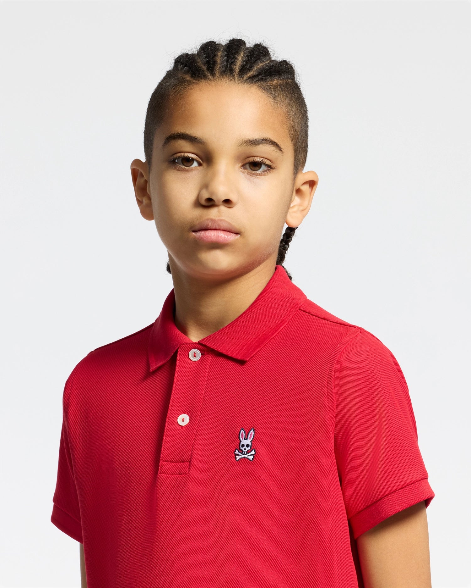 Vibrant red kids classic pique polo shirt, featuring a classic fit, two white button placket, and a small, multi-color embroidered Psycho Bunny skull logo on the left chest.