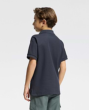 A young boy with short brown hair, seen from behind, is wearing a Psycho Bunny KIDS CLASSIC PIQUE POLO SHIRT - B0K001CRPC in dark navy and green cargo shorts, set against a plain light background.