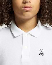 A person with curly hair is wearing a Psycho Bunny KIDS CLASSIC PIQUE POLO SHIRT in soft Pima cotton, adorned with a small pink bunny logo and crossbones on the left side. The image shows their upper torso and face, excluding the eyes.