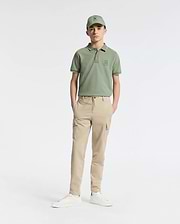 A teen boy wears a Psycho Bunny green cap and polo shirt, KIDS GREEN VALLEY CARGO PANT - B0P199E200 with ample pockets, and white sneakers while standing comfortably against a plain white background with hands in pockets.