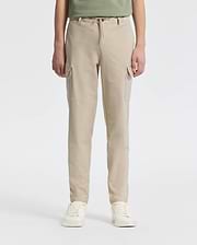 A person stands against a plain backdrop wearing Psycho Bunny’s KIDS GREEN VALLEY CARGO PANT - B0P199E200, featuring beige drawstring waist and multiple pockets, paired with white sneakers. The upper body is partially visible.