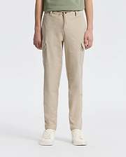 A person stands against a plain backdrop wearing Psycho Bunny’s KIDS GREEN VALLEY CARGO PANT - B0P199E200, featuring beige drawstring waist and multiple pockets, paired with white sneakers. The upper body is partially visible.