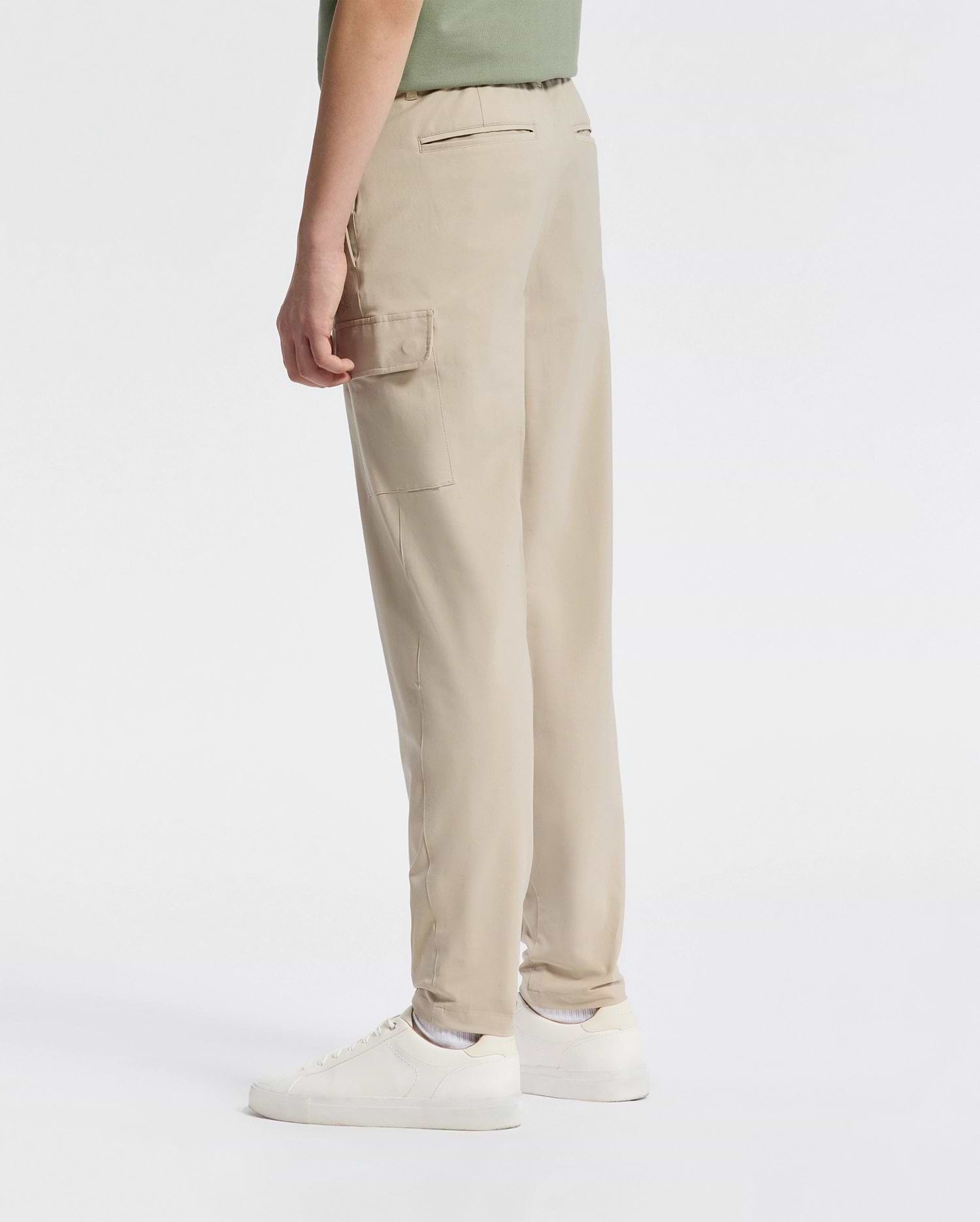 A person wearing Psycho Bunny's Kids Green Valley Cargo Pant (B0P199E200) with side pockets, paired with white sneakers, stands sideways against a plain white background. They're dressed in a green top that's partially visible.