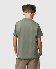 A young boy with short brown hair faces away, wearing a Psycho Bunny Kids Classic Crew Neck Tee in plain green and beige shorts. This 100% Pima cotton tee is ideal for back-to-school, set against a light grey background.
