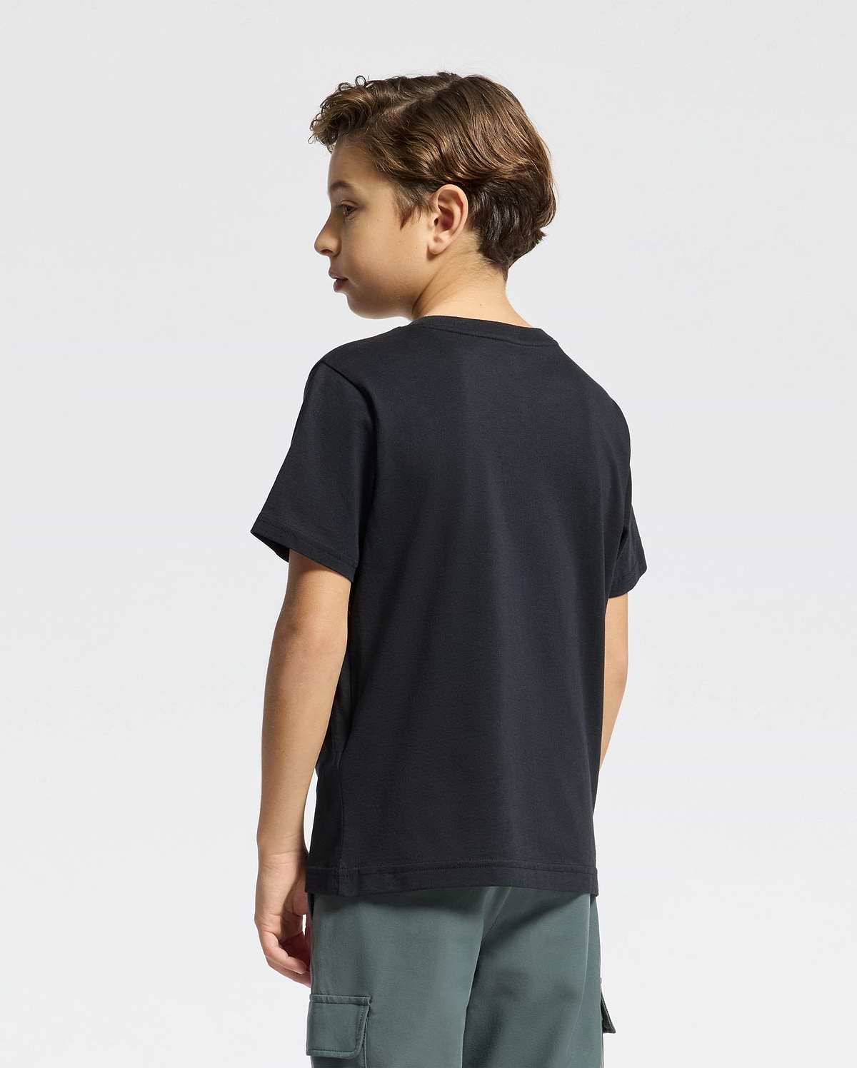 A young boy with short hair stands sideways, sporting a Psycho Bunny KIDS CLASSIC CREW NECK TEE - B0U014CRPC in black and green cargo shorts against a plain white background.