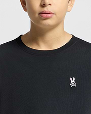 A person wearing the Psycho Bunny KIDS CLASSIC CREW NECK TEE - B0U014CRPC in classic black, made from 100% Pima cotton, features a chest logo with a pink-eared rabbit and crossbones on a plain light-colored background.