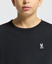 A person wearing the Psycho Bunny KIDS CLASSIC CREW NECK TEE - B0U014CRPC in classic black, made from 100% Pima cotton, features a chest logo with a pink-eared rabbit and crossbones on a plain light-colored background.