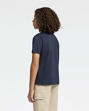 A person wears a Psycho Bunny Kids Classic Crew Neck Tee in navy blue with beige cargo pants, standing sideways with arms relaxed, looking left. Their curly hair enhances the casual vibe against a plain light background. This tee's Pima cotton offers both comfort and style effortlessly.