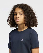 A curly-haired person wears a navy Psycho Bunny KIDS CLASSIC CREW NECK TEE - B0U014CRPC, made from 100% Pima cotton, showcasing a small pink bunny with crossbones on the chest, standing out against the white background.