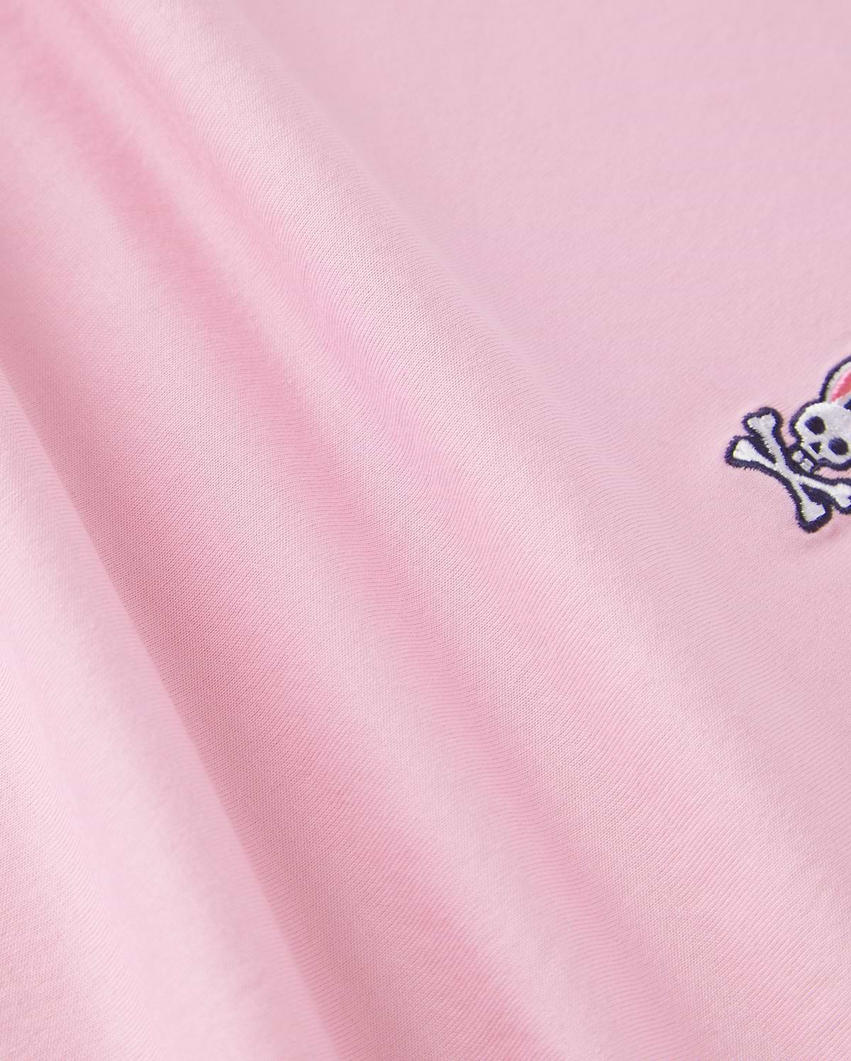 The Psycho Bunny KIDS CLASSIC CREW NECK TEE - B0U014CRPC is made of 100% Pima cotton, showcasing a pink fabric with an embroidered skull and crossbones. It offers a smooth texture and soft look, ideal for back-to-school outfits.