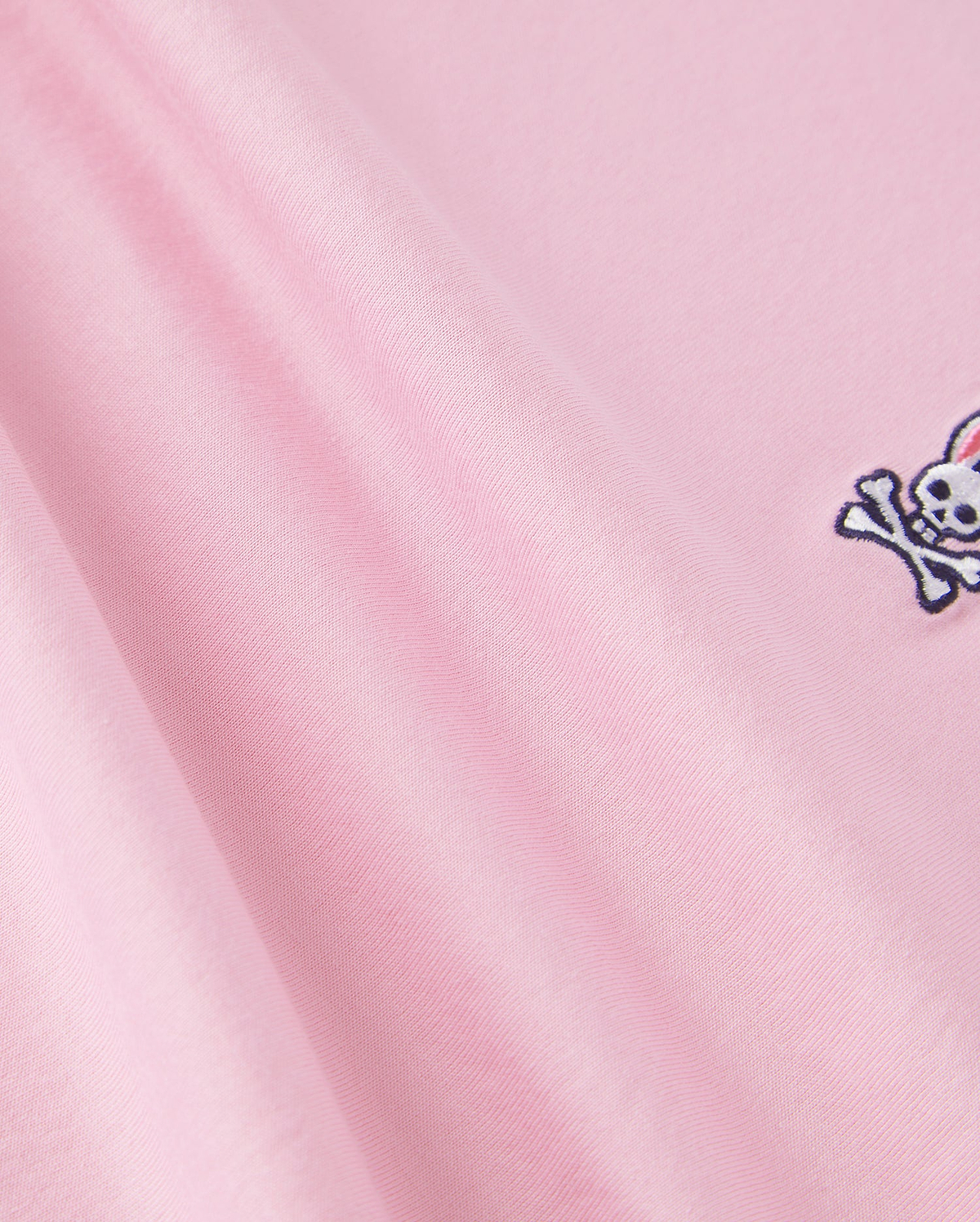 The Psycho Bunny KIDS CLASSIC CREW NECK TEE - B0U014CRPC is made of 100% Pima cotton, showcasing a pink fabric with an embroidered skull and crossbones. It offers a smooth texture and soft look, ideal for back-to-school outfits.