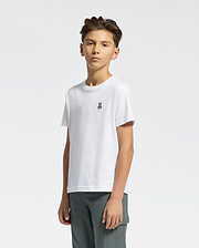 A young person with short brown hair wears the KIDS CLASSIC CREW NECK TEE by Psycho Bunny, showcasing the embroidered Classic Psycho Bunny logo, paired with dark green pants against a plain light background.