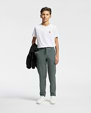 A young person stands against a plain background, wearing the Psycho Bunny KIDS CLASSIC CREW NECK TEE, green cargo pants, and white sneakers. They hold a black jacket on their shoulder, subtly nodding to the Classic Psycho Bunny logo.