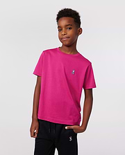 A boy stands confidently with one hand in his pocket, wearing Psycho Bunny’s KIDS CLASSIC CREW NECK TEE (B0U014CRPC) in premium Pima cotton with an embroidered logo and black pants, set against a plain light background.