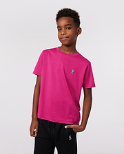 A boy stands confidently with one hand in his pocket, wearing Psycho Bunny’s KIDS CLASSIC CREW NECK TEE (B0U014CRPC) in premium Pima cotton with an embroidered logo and black pants, set against a plain light background.