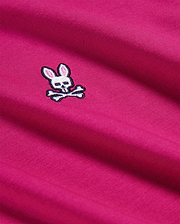 A close-up of the KIDS CLASSIC CREW NECK TEE - B0U014CRPC by Psycho Bunny in magenta premium Pima cotton, featuring an embroidered white bunny logo with pink ears and a skull face above crossed bones.