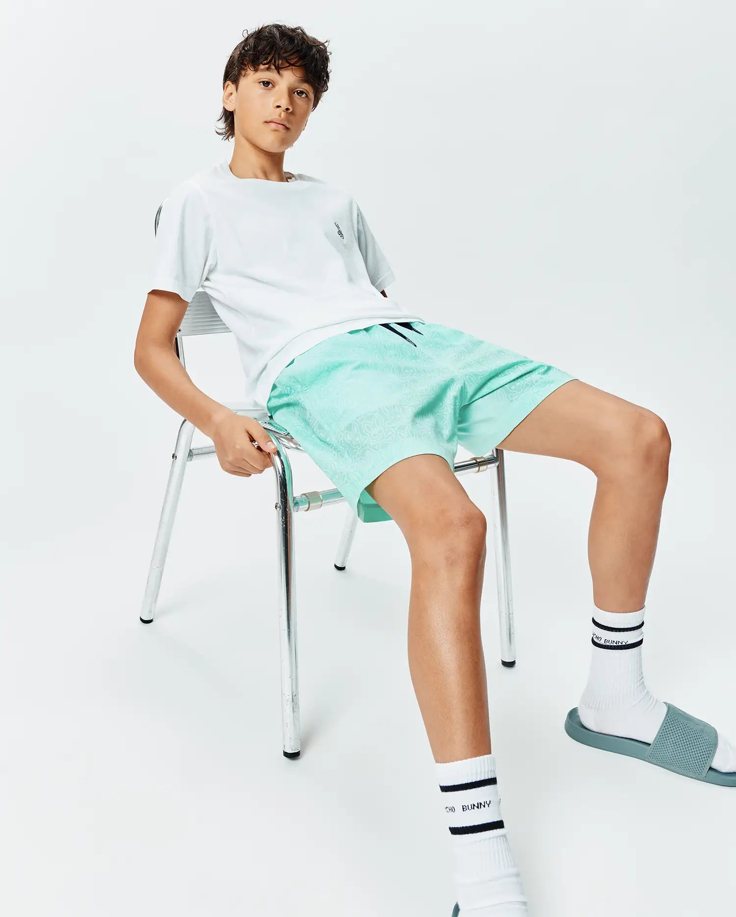 Kids Samos Hydrochromic Printed Swim Trunk in mint green with a subtle all-over Psycho Bunny skull pattern, paired with a white jersey t-shirt featuring a small chest logo. (4)