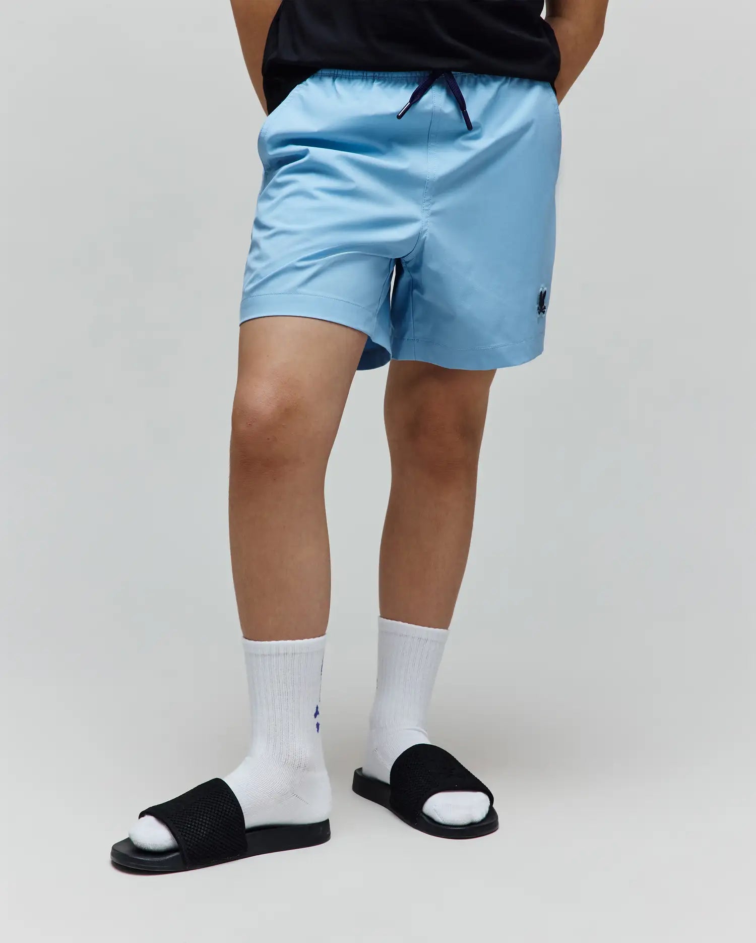 Kids Samos Hydrochromic Printed Swim Trunk in light blue, featuring a relaxed fit, smooth quick-dry fabric, elastic waistband with navy drawstring, and a small embroidered Psycho Bunny skull logo on the left leg.
