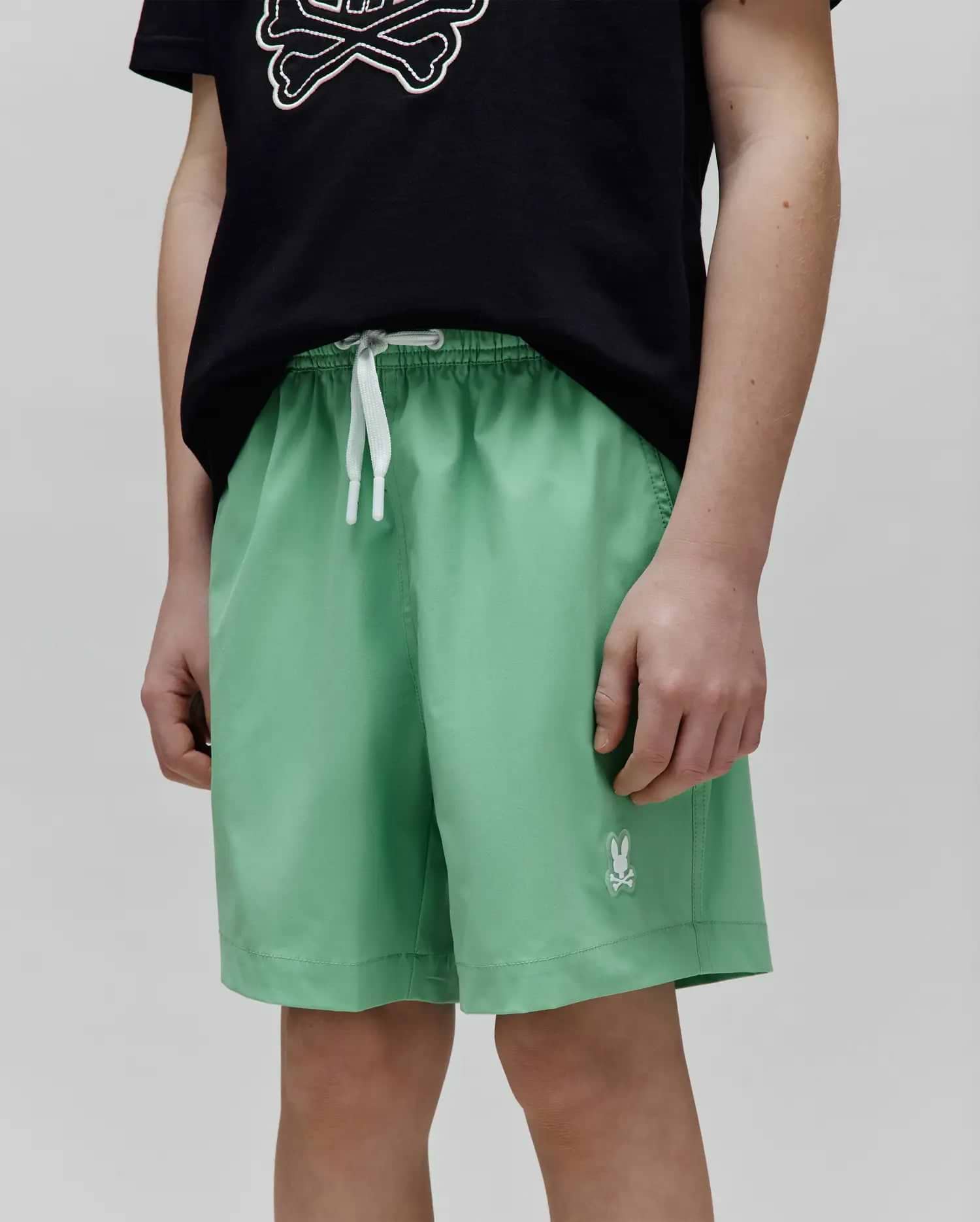 Kids Samos Hydrochromic Printed Swim Trunk in light green, featuring a relaxed fit, smooth fabric, white drawstrings, and a small embroidered white Psycho Bunny skull logo on the left leg.