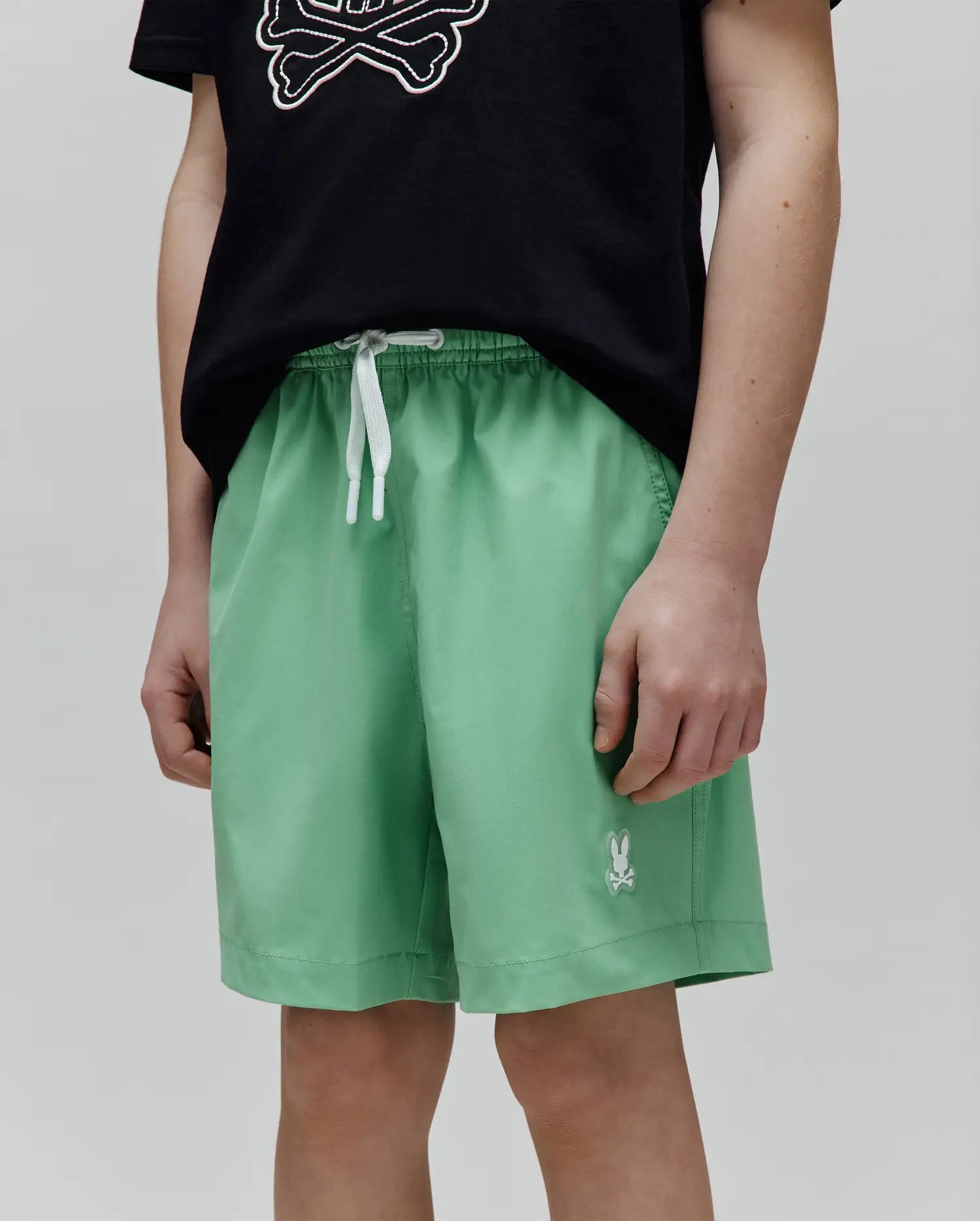 Kids Samos Hydrochromic Printed Swim Trunk in light green, featuring a relaxed fit, smooth fabric, white drawstrings, and a small embroidered white Psycho Bunny skull logo on the left leg.