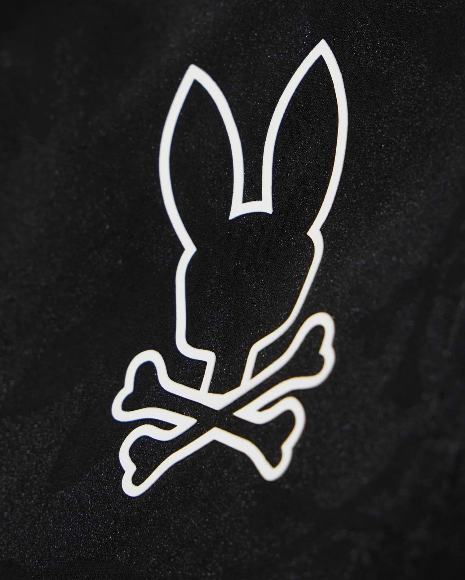 A black background with a white graphic design featuring the silhouette of a bunny's head, complete with large upright ears, positioned above two crossed bones. Perfect for customizing your waterproof bag or Psycho Bunny KIDS PARKER HYDROCHROMIC SWIM TRUNK - B0W646C200.