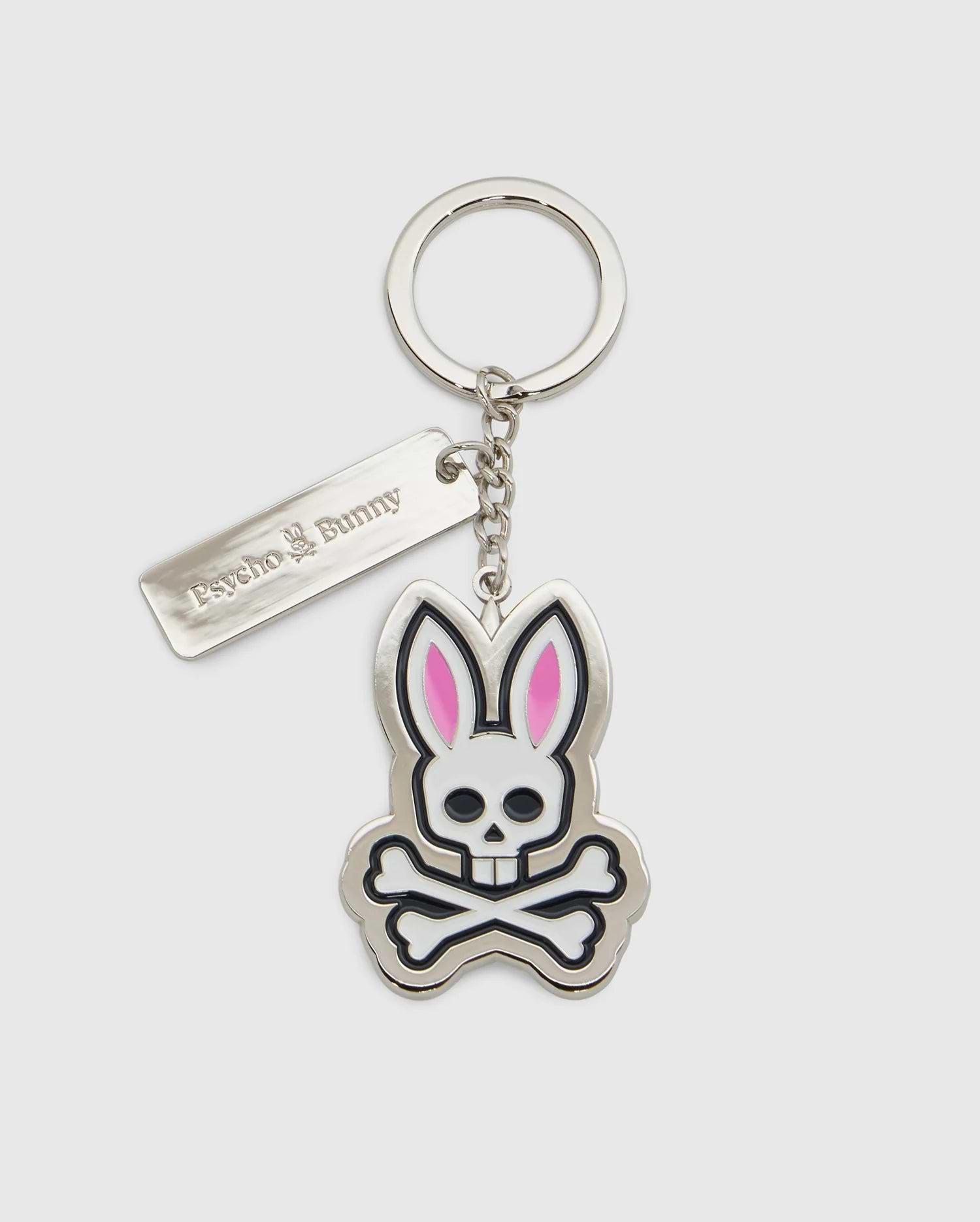 Introducing the CLASSIC BUNNY KEYCHAIN - B6A372E200 from Psycho Bunny, a fashionable metal accessory showcasing a cartoon bunny skull and crossbones design with distinctive pink ears. This practical everyday keychain features a sleek rectangular tag engraved with "Psycho Bunny." Complemented by a silver-colored chain and keyring, it adds a chic touch to your essentials.