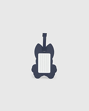 A navy blue luggage tag in the shape of a cat is pictured. The front side features a rectangular white label with blank lines for writing contact information. Made from detachable silicone, the Psycho Bunny MENS LUGGAGE TAG - B6A387B200 has a strap at the top for attaching to luggage.