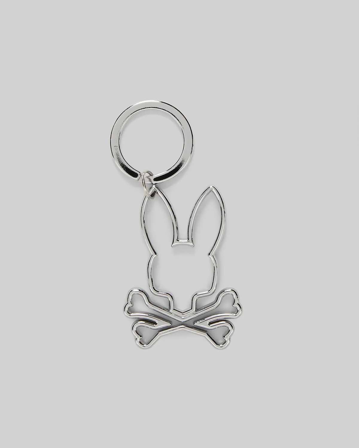 The Psycho Bunny MENS OUTLINE BUNNY KEYCHAIN (B6A565E200) is a durable silver accessory featuring a rabbit head over crossed bones, crafted from zinc alloy and set on a plain gray background.