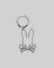 The Psycho Bunny MENS OUTLINE BUNNY KEYCHAIN (B6A565E200) is a durable silver accessory featuring a rabbit head over crossed bones, crafted from zinc alloy and set on a plain gray background.