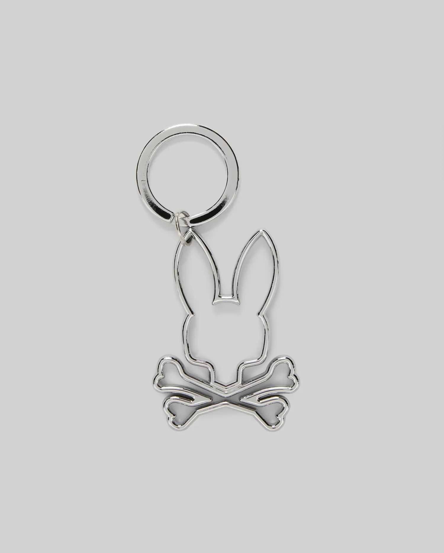 The Psycho Bunny MENS OUTLINE BUNNY KEYCHAIN (B6A565E200) is a durable silver accessory featuring a rabbit head over crossed bones, crafted from zinc alloy and set on a plain gray background.