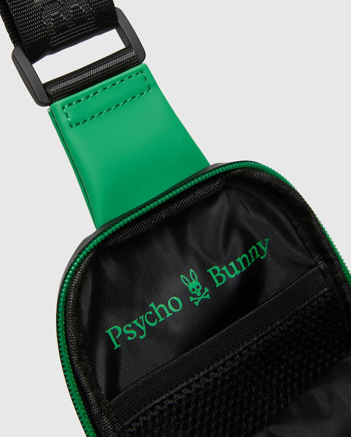 Black Mens Rubberized Crossbody with a vibrant green rubberized strap accent, green zipper, and prominent green Psycho Bunny skull logo inside the black woven interior.