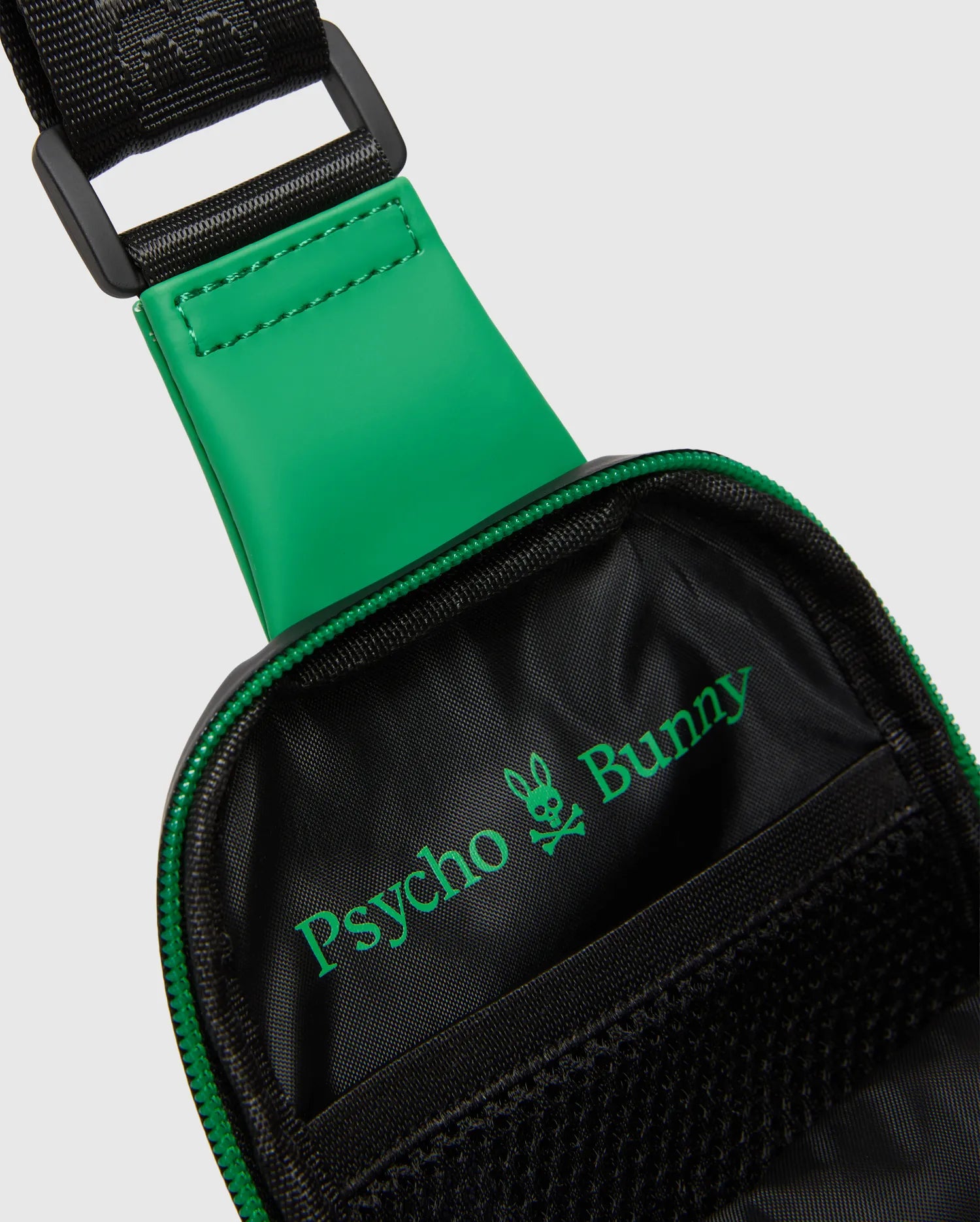 Black Mens Rubberized Crossbody with a vibrant green rubberized strap accent, green zipper, and prominent green Psycho Bunny skull logo inside the black woven interior.