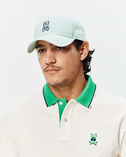 Cream pique polo with green collar, navy stripe, and embroidered Psycho Bunny logo with sunglasses, paired with a mint Mens Classic Baseball Cap featuring an embroidered bunny skull.