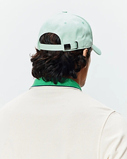 Mint Green Mens Classic Baseball Cap with a small Psycho Bunny skull logo on the metal buckle, paired with a cream pique polo featuring a green ribbed collar and thin navy stripe.