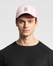A young person sports Psycho Bunny's MENS CLASSIC BASEBALL CAP - B6A816A1HT made of cotton twill with an embroidered bunny and crossbones logo. Their black shirt features the same playful design, standing out against the plain background.