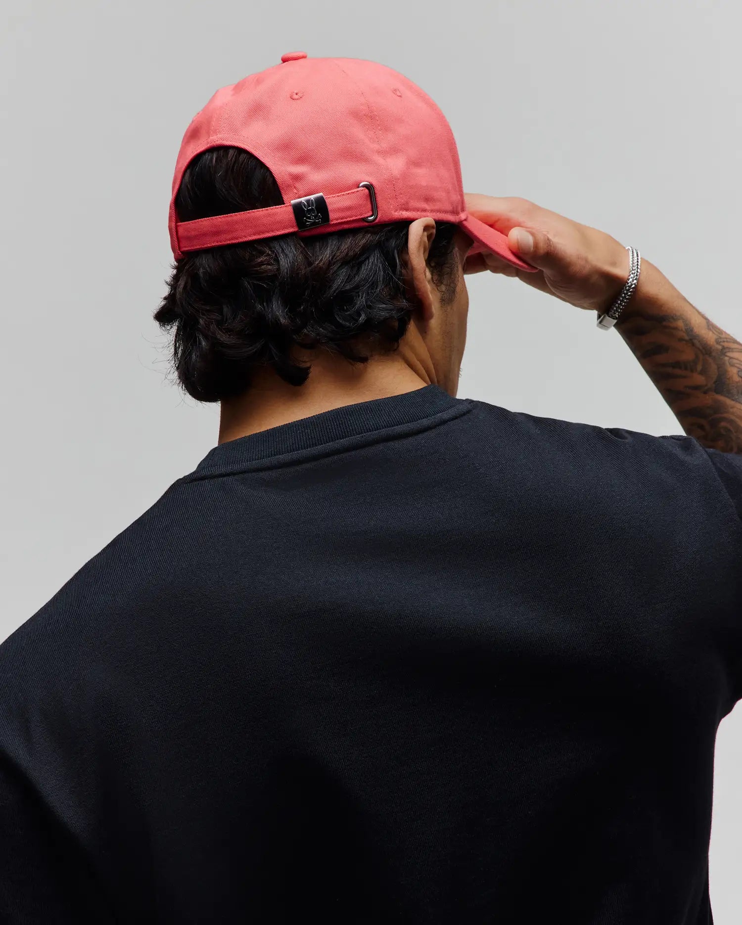 Mens Classic Baseball Cap in vibrant coral, featuring an adjustable strap with a metallic Psycho Bunny skull logo, worn with a classic fit black jersey crewneck t-shirt. (3)