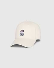 The Psycho Bunny MENS CLASSIC BASEBALL CAP (B6A816B200), made from 100% cotton in beige, showcases a small pink bunny with crossed bones on the front. Angled to highlight both front and side, this standout accessory adds character to any collection.
