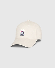 The Psycho Bunny MENS CLASSIC BASEBALL CAP (B6A816B200), made from 100% cotton in beige, showcases a small pink bunny with crossed bones on the front. Angled to highlight both front and side, this standout accessory adds character to any collection.
