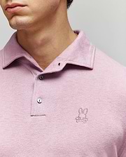 A man wears the Psycho Bunny MENS BRADSHAW POLO SWEATER (B6E835D200) in light purple, featuring a small embroidered bunny and crossbones logo on the chest and mother of pearl buttons against a neutral background. (2)