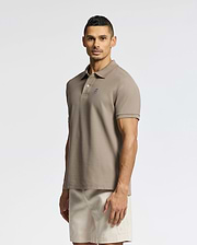 A man stands against a plain background, wearing a Psycho Bunny MENS CLASSIC PIQUE POLO SHIRT - B6K001CRPC with a small chest logo and light beige shorts. He faces forward with a neutral expression.