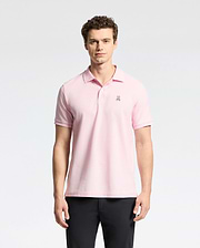 A man stands against a white background, wearing Psycho Bunny's light pink Mens Classic Pique Polo Shirt (B6K001CRPC) made of Peruvian pima cotton with a small chest emblem. He has curly hair, looks directly at the camera, and is also dressed in black pants.