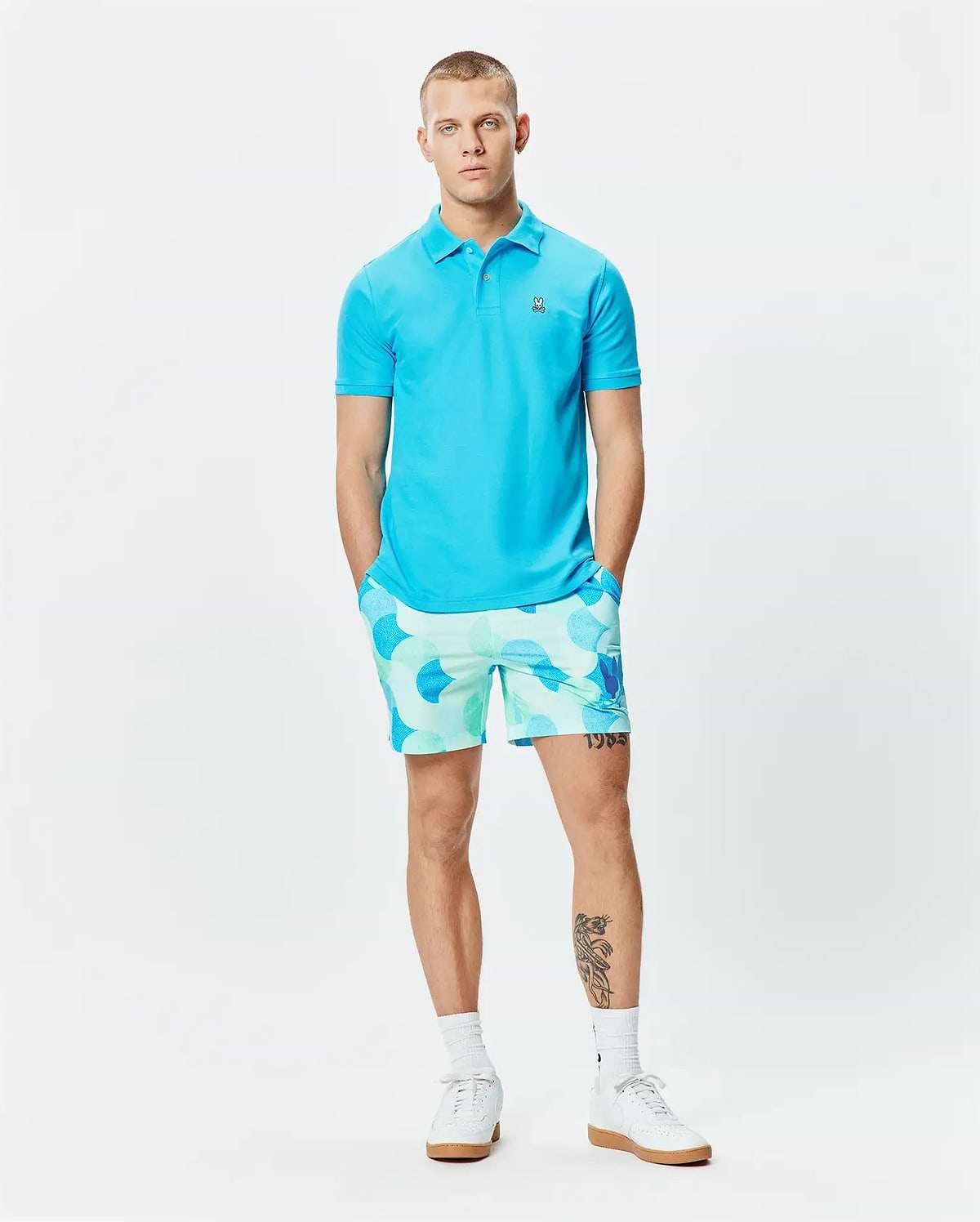 Mens Classic Pique Polo in vibrant cyan, featuring a classic fit and small embroidered Psycho Bunny skull logo on the left chest. Paired with relaxed-fit shorts in a light blue and mint green all-over circular pattern. (6)