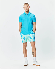 Mens Classic Pique Polo in vibrant cyan, featuring a classic fit and small embroidered Psycho Bunny skull logo on the left chest. Paired with relaxed-fit shorts in a light blue and mint green all-over circular pattern. (6)